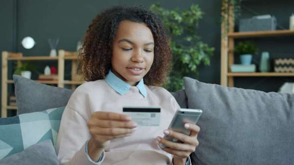 Young woman holding credit card and smartphone indoors