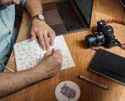man writing on paper in front of DSLR